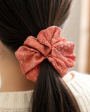 Close-up of the Coral Gold Fleck kimono scrunchie worn on a low ponytail